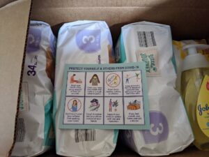 Image description: a photo of a box of diaper packs and a postcard with Covid-19 precautions